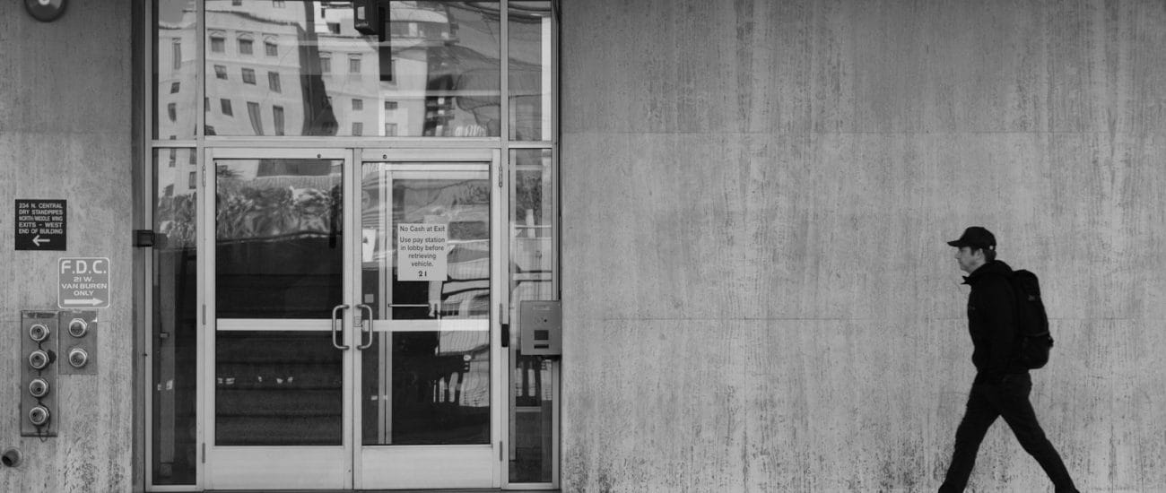 Person walking past a concrete building in black and white