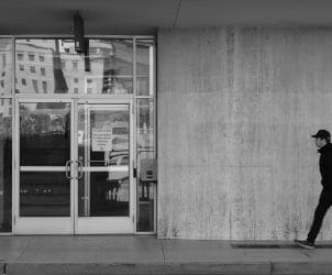 Person walking past a concrete building in black and white