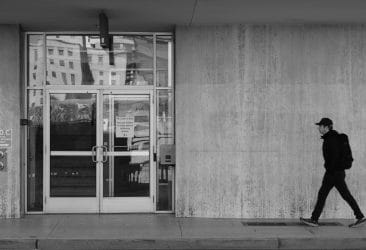 Person walking past a concrete building in black and white