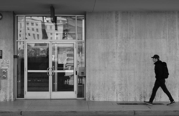 Person walking past a concrete building in black and white